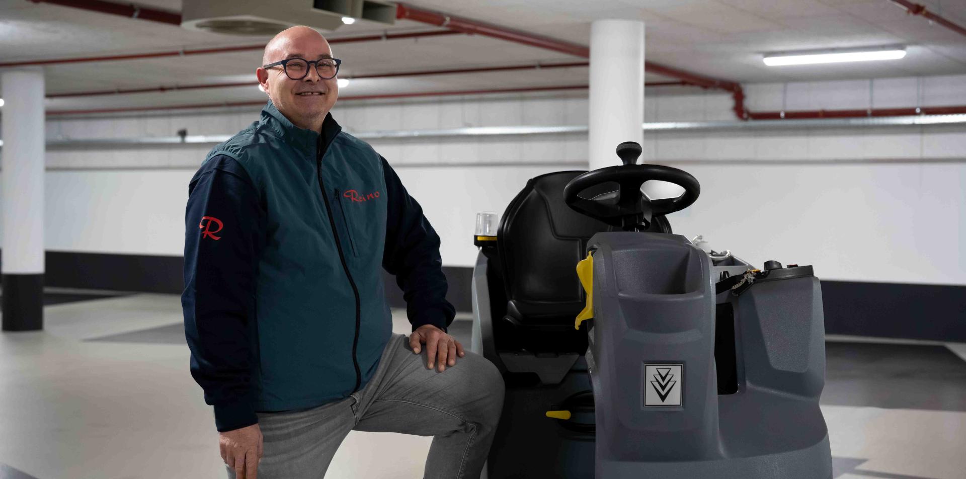 Reino medewerker staat naast een rijdende veegmachine in een parkeergarage