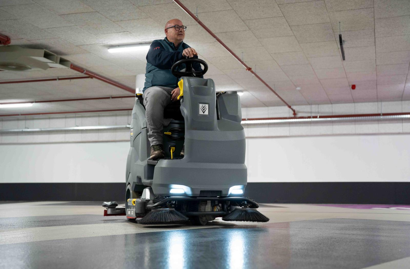 Reino medewerker rijdt op een professionele veegmachine in een parkeergarage