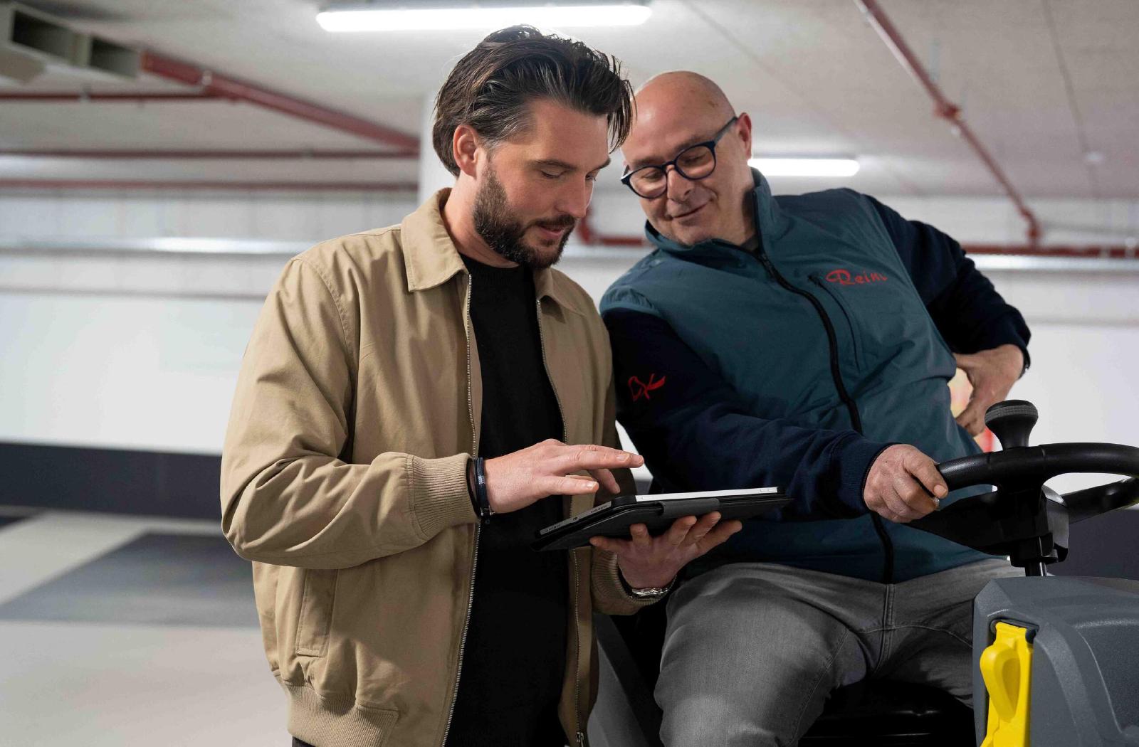 Yannick Nieuwenhoven en een Reino medewerker bekijken een tablet bij een veegmachine