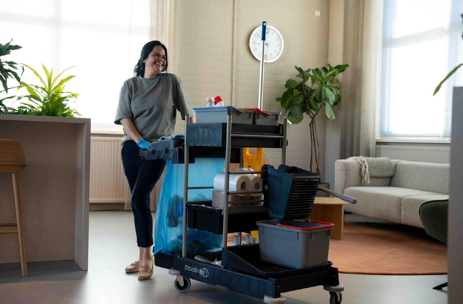 Reino schoonmaakmedewerkster met volgeladen schoonmaakwagen in kantoorruimte
