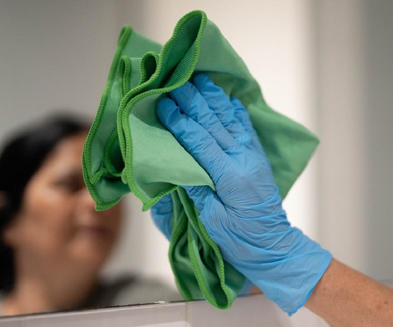 Handen met microvezeldoek en handschoenen reinigen een spiegel