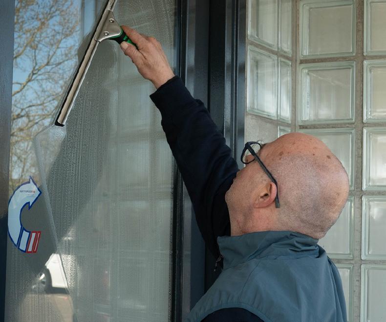 Reino medewerker wast een glazen deur schoon met een raamafreker