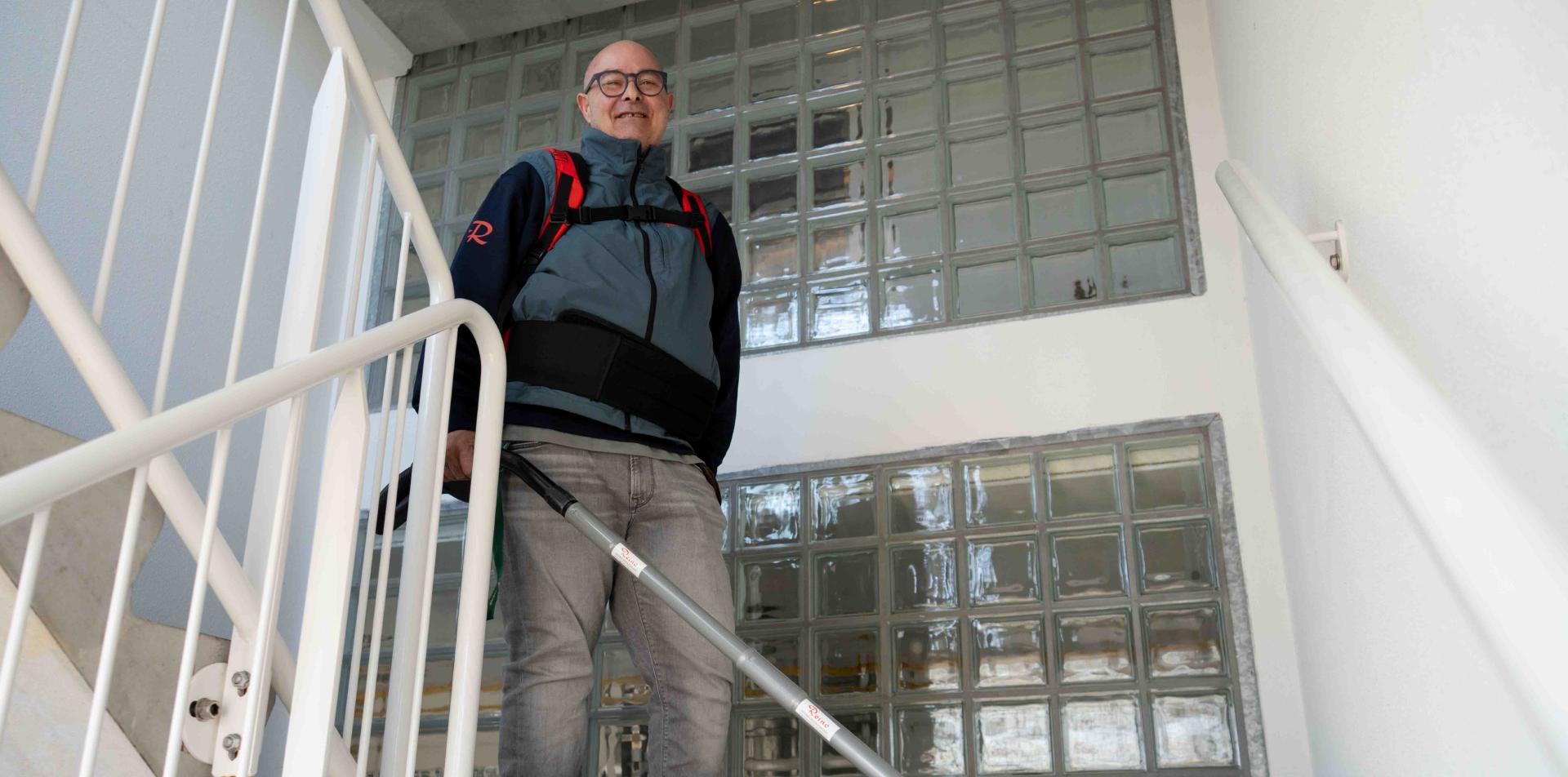 Reino medewerker met rugzak stofzuiger op een trap bij glasblokken wand