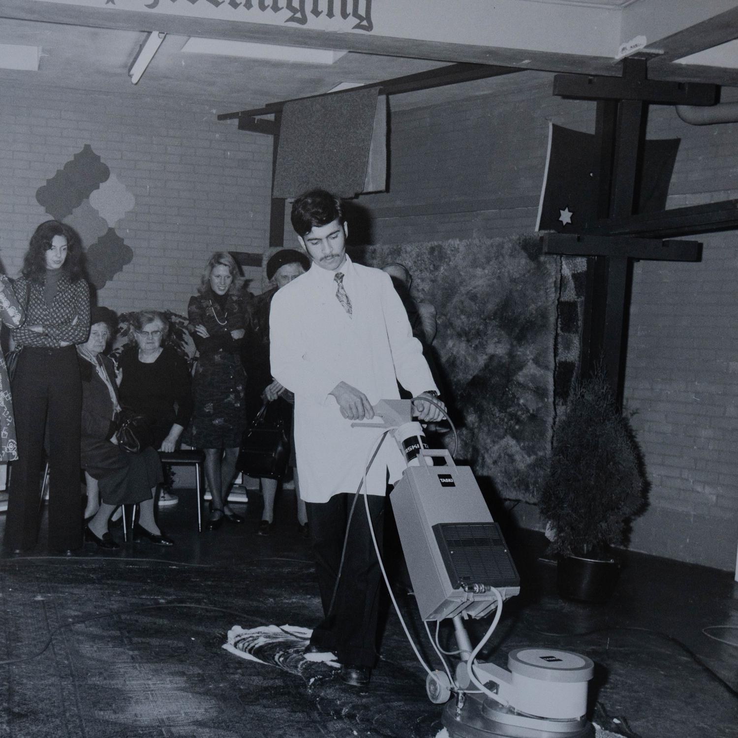 Historische zwart-witfoto van een tapijtreinigingsdemonstratie in een showroom, jaren zestig