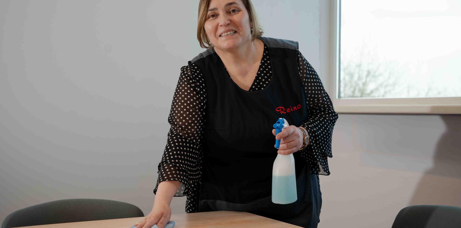 Reino schoonmaakmedewerkster maakt een tafel schoon in een vergaderruimte