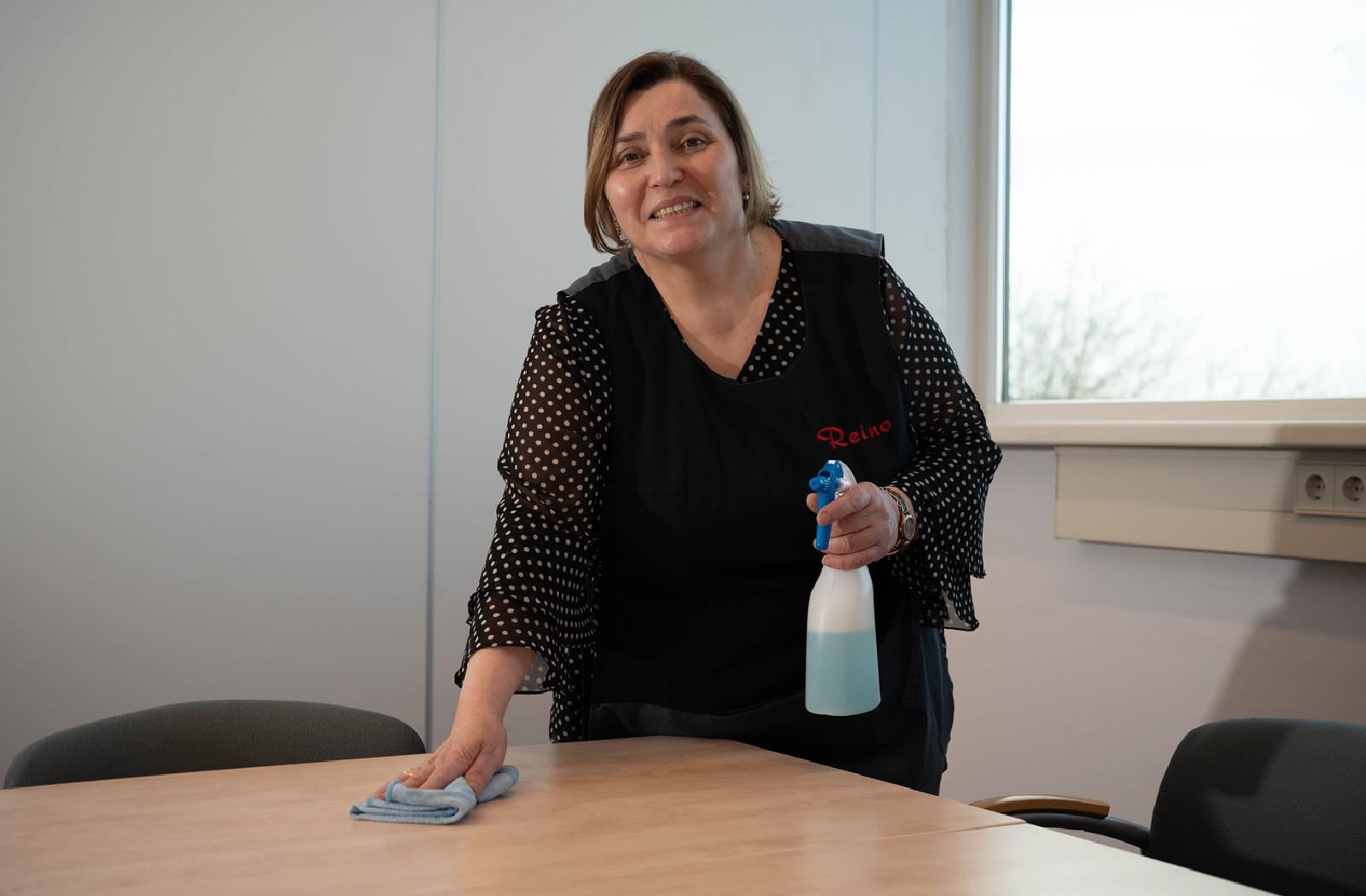 Reino schoonmaakmedewerkster reinigt een tafel in een kantoor