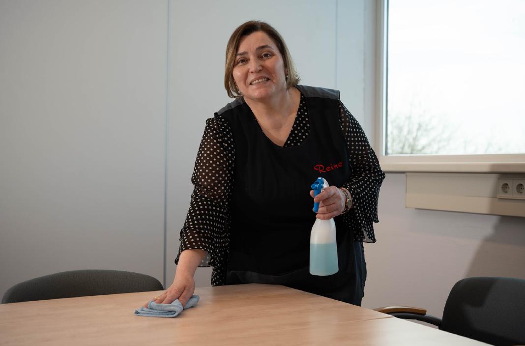 Reino schoonmaakmedewerkster reinigt een tafel in een kantoor
