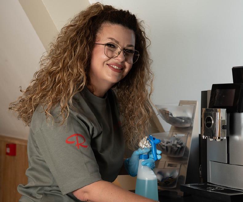 Reino schoonmaakmedewerkster reinigt een koffiezetapparaat op kantoor