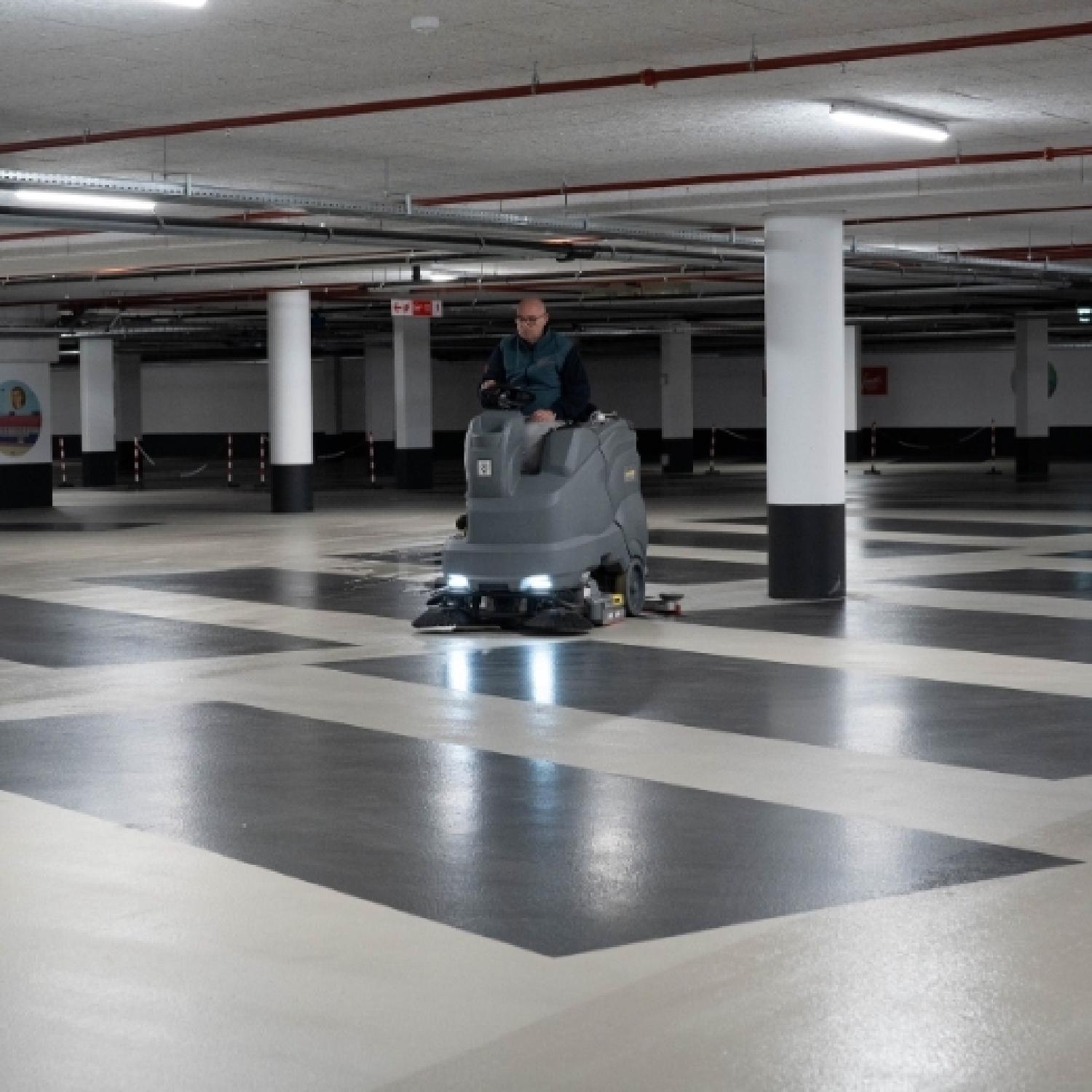 Reino medewerker rijdt met een veegmachine over de vloer van een grote parkeergarage